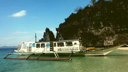 Bateau de plongée amarré dans une crique turquoise face à une falaise