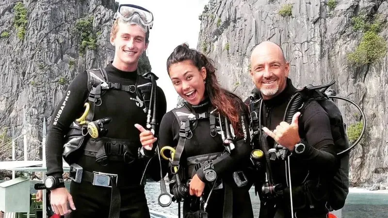 Trois plongeurs souriants en combinaison, équipés sur un bateau en mer