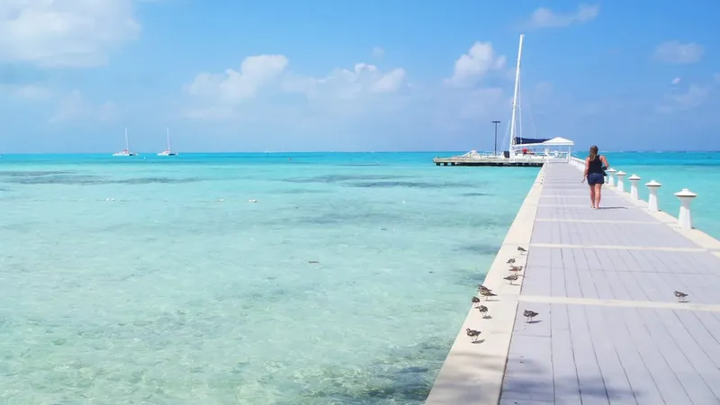 Une femme marche sur un ponton au-dessus d'une eau turquoise claire
