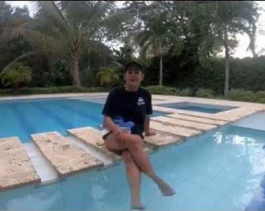 Une personne assise au bord d'une piscine avec végétation luxuriante