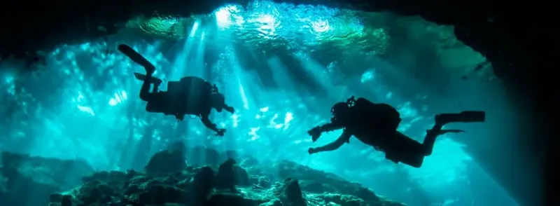 Deux plongeurs explorent une grotte sous-marine éclairée par des rayons de soleil
