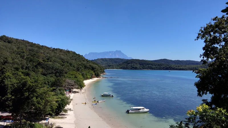 Plage de sable blanc avec bateaux et personnes sous un ciel bleu