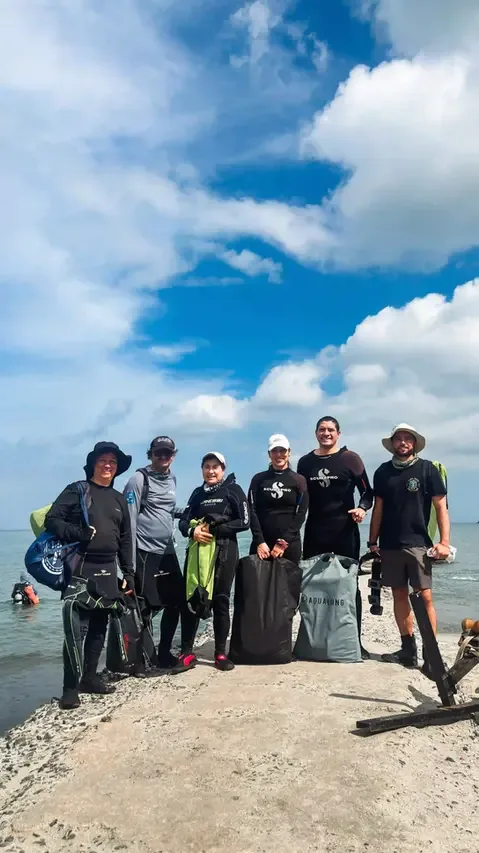 Groupe de plongeurs souriants sur une plage ensoleillée avec équipement