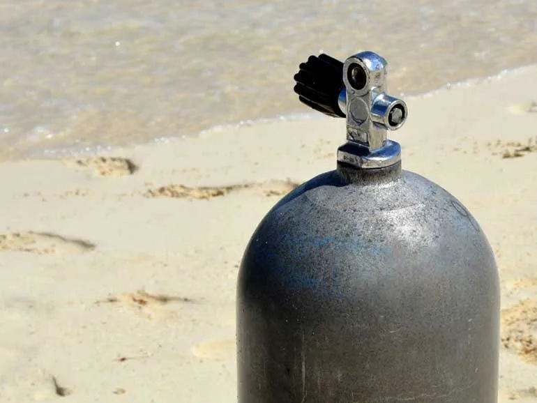 Bouteille de plongée noire sur sable clair avec vannes métalliques