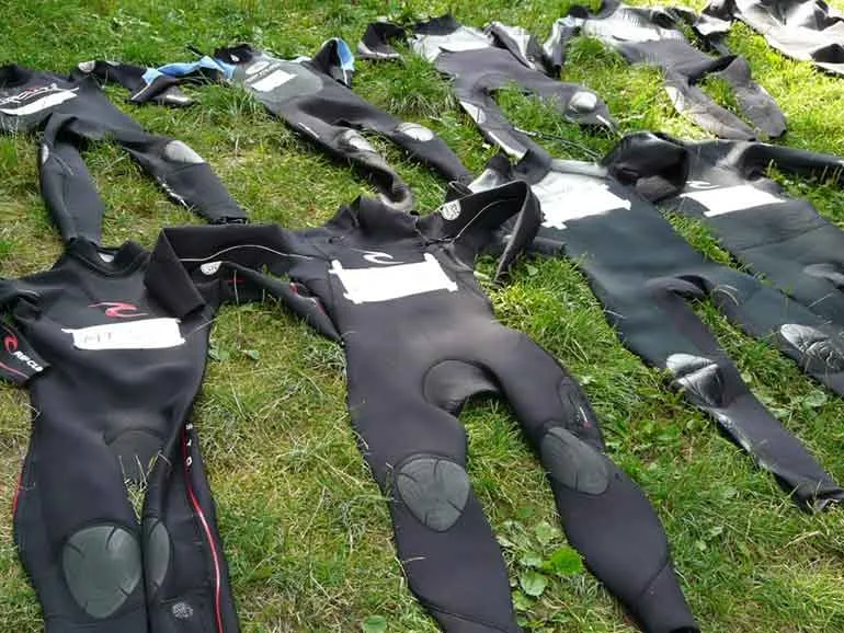 Combinaisons de plongée noires étalées sur l'herbe, séchant au soleil