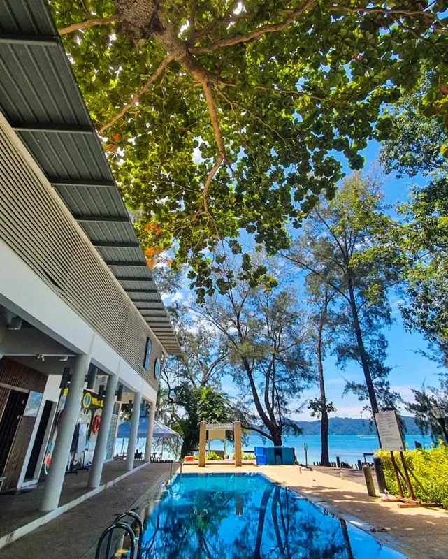 Bâtiment blanc avec piscine, arbres et vue sur la mer en arrière-plan