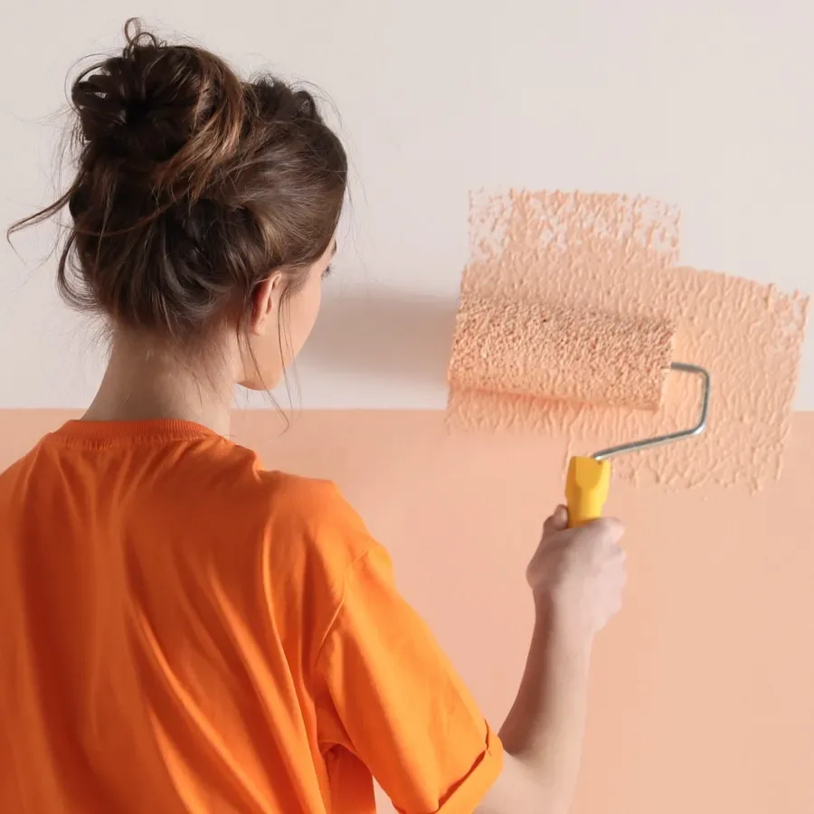 Une femme peint un mur dans une teinte pêche pastel