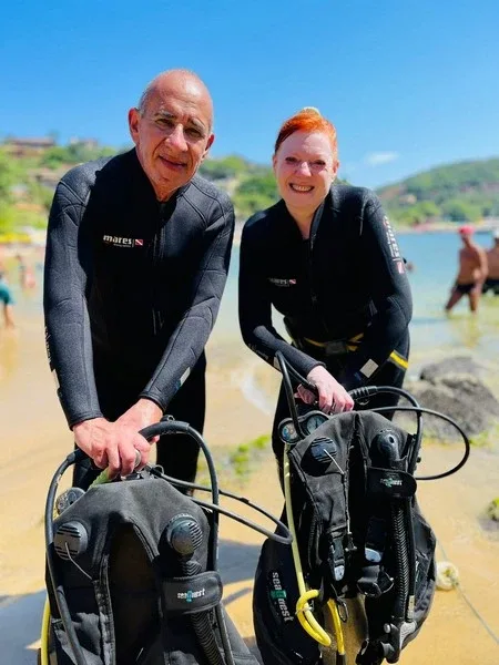 Deux plongeurs souriants en combinaison avec leur équipement sur une plage