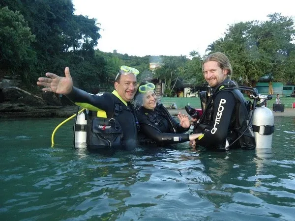 Trois plongeurs souriants en combinaison dans l'eau, équipés de bouteilles