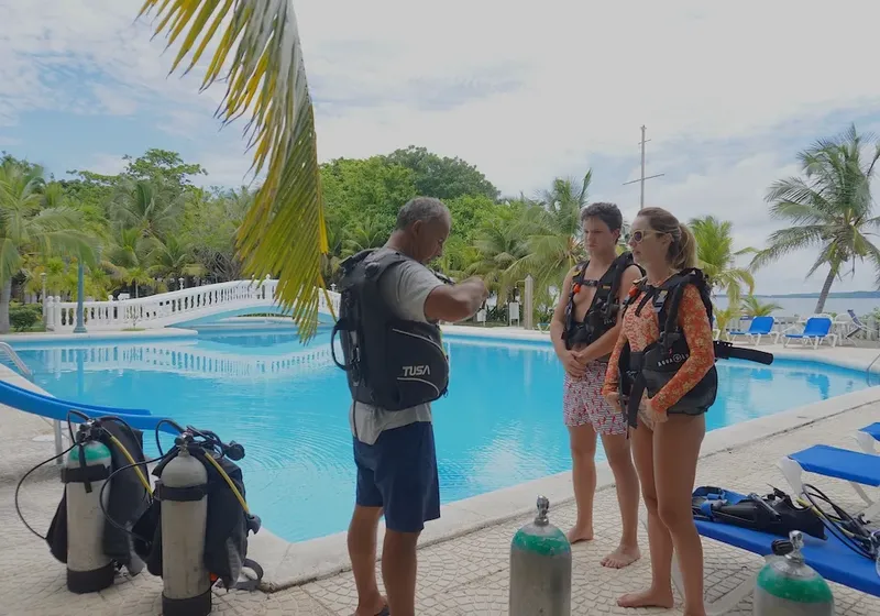 Instructeur expliquant l'équipement de plongée à deux élèves près d'une piscine