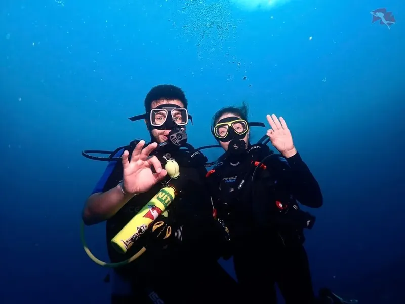 Deux plongeurs souriants font signe avec la main dans l'eau bleue