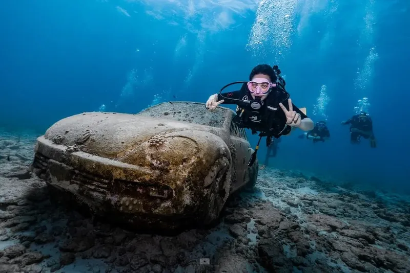 Plongeuse souriante fait un signe de paix devant une voiture sous marine