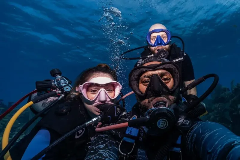 Trois plongeurs souriants se prennent en selfie sous l'eau