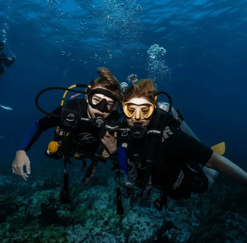 Deux plongeurs souriants, équipés, nagent ensemble dans l'eau bleue
