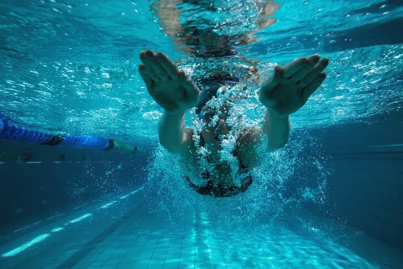 nageur sous l'eau, vue d'en bas, mains tendues, piscine bleue