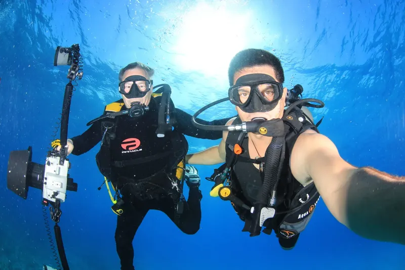 Deux plongeurs souriants prennent un selfie sous l'eau en combinaison