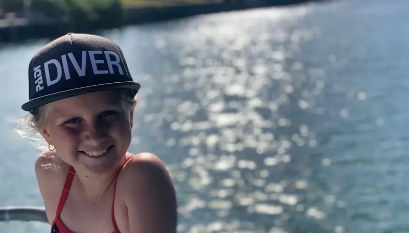 Jeune plongeuse souriante portant une casquette avec l'inscription DIVER