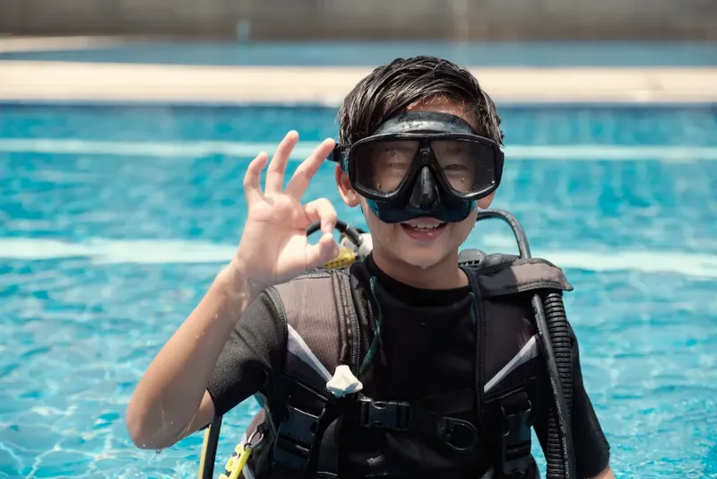 Jeune plongeur souriant avec signe OK, équipé en surface piscine