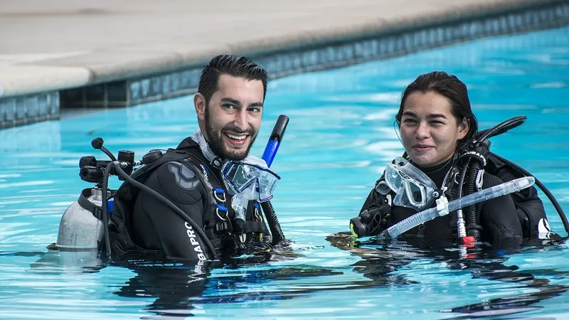 Deux plongeurs souriants en combinaison dans une piscine bleu turquoise