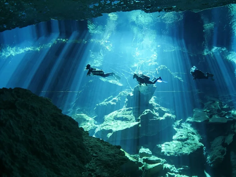 Trois plongeurs explorent une grotte sous-marine éclairée par des rayons