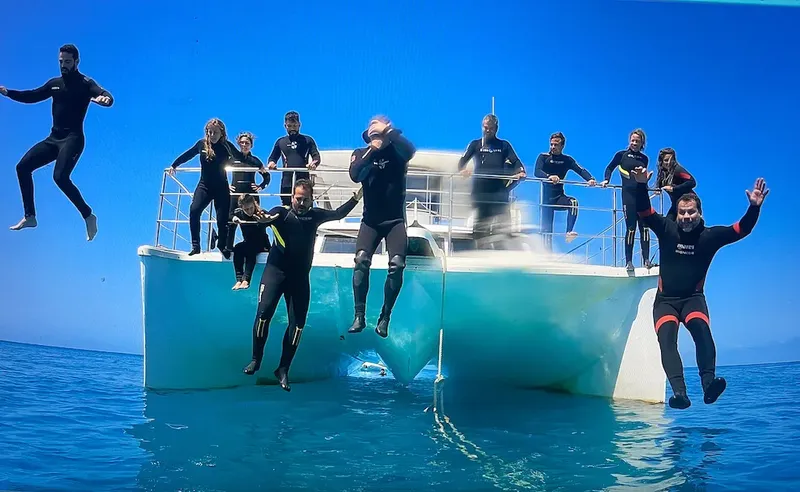 Groupe de personnes en combinaisons de plongée sautant d'un catamaran bleu