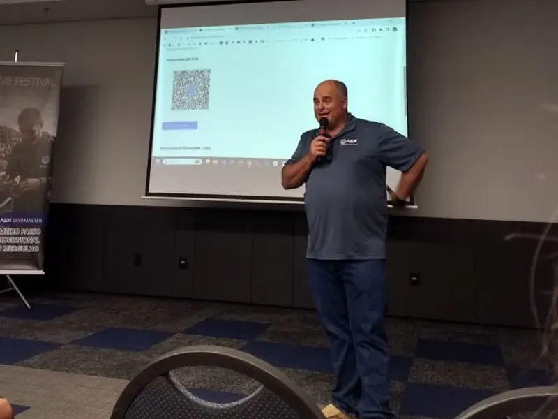 Un homme parle avec un micro devant un écran de projection