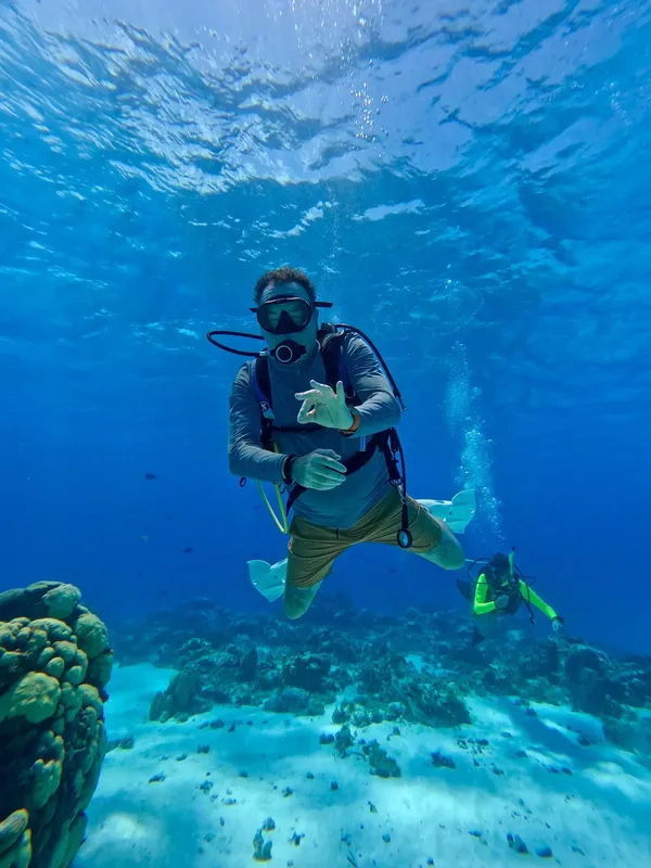Plongeur en combinaison regarde sa montre sous l'eau avec corail