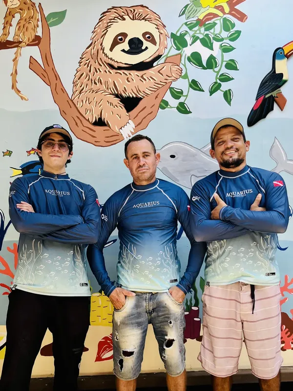 Trois personnes souriantes posent devant une fresque marine colorée