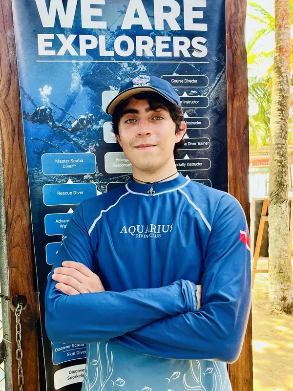 Jeune homme souriant devant une affiche de niveaux de plongée