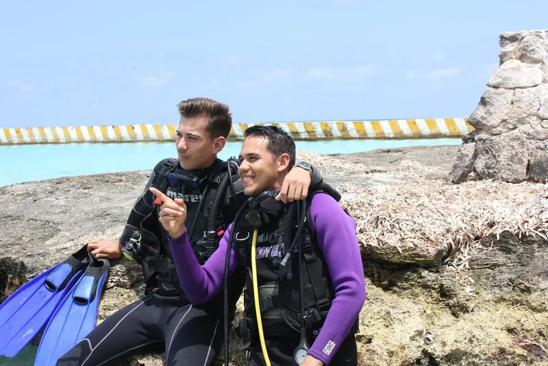 Deux plongeurs souriants équipés sur un rocher en bord de mer