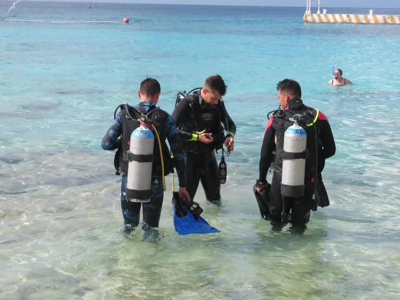 Trois plongeurs équipés se préparent à entrer dans une mer turquoise