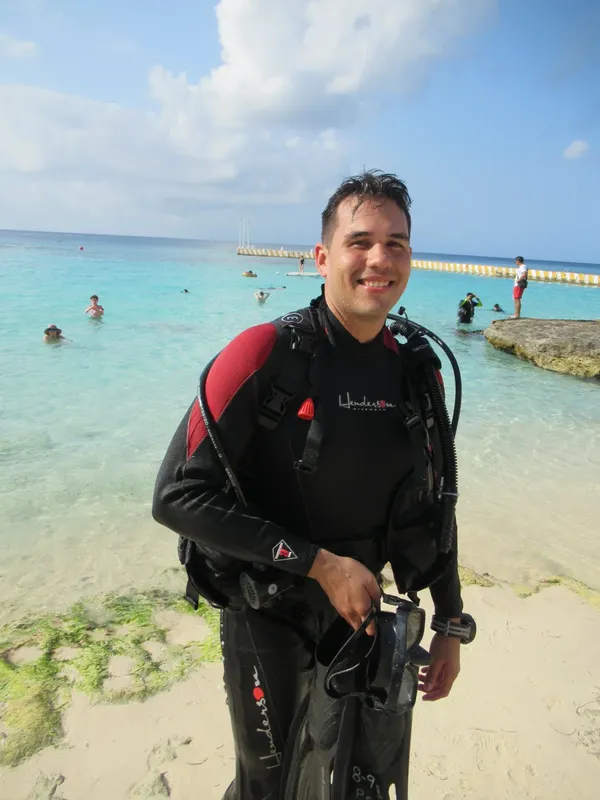 Plongeur souriant sur une plage, équipé de son matériel de plongée