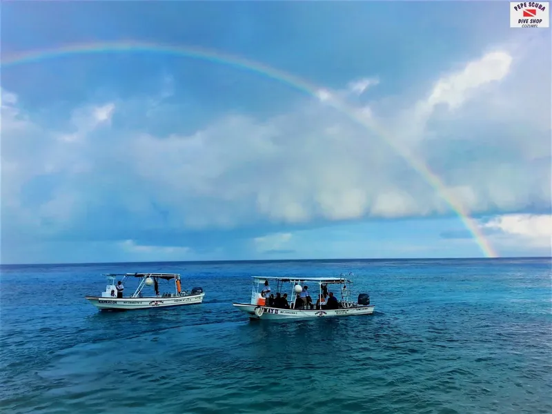 Deux bateaux de plongée naviguent sur une mer calme sous un arc-en-ciel