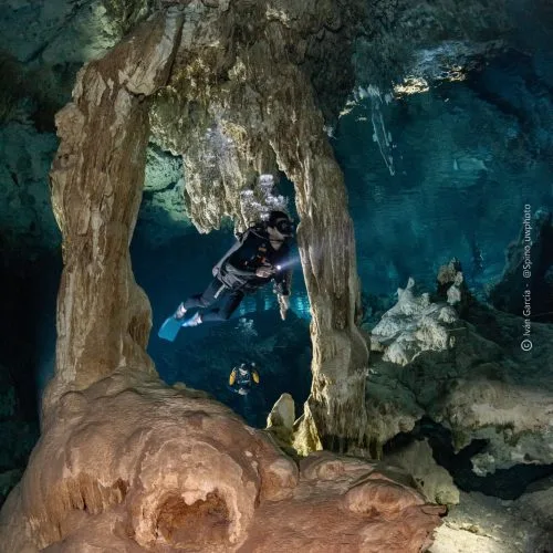 Deux plongeurs explorent une grotte sous-marine rocheuse et illuminée