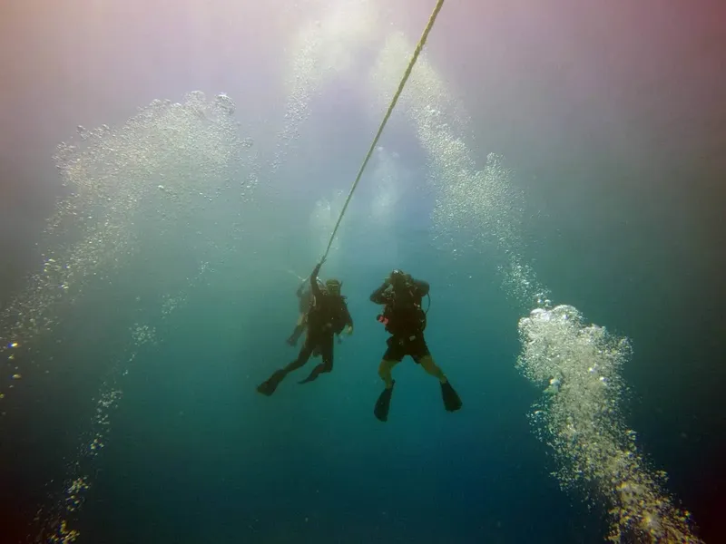 Deux plongeurs remontent le long d'un câble dans l'eau bleue