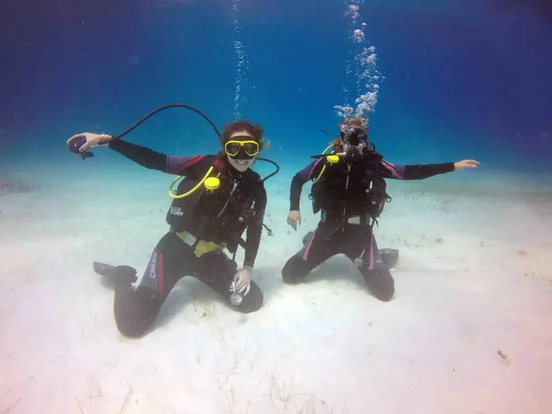 Deux plongeurs souriants posent sur le fond sableux en mer