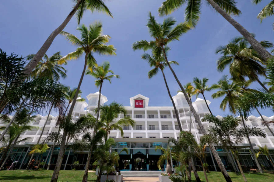 Bâtiment blanc avec logo rouge RIU, entouré de palmiers au soleil