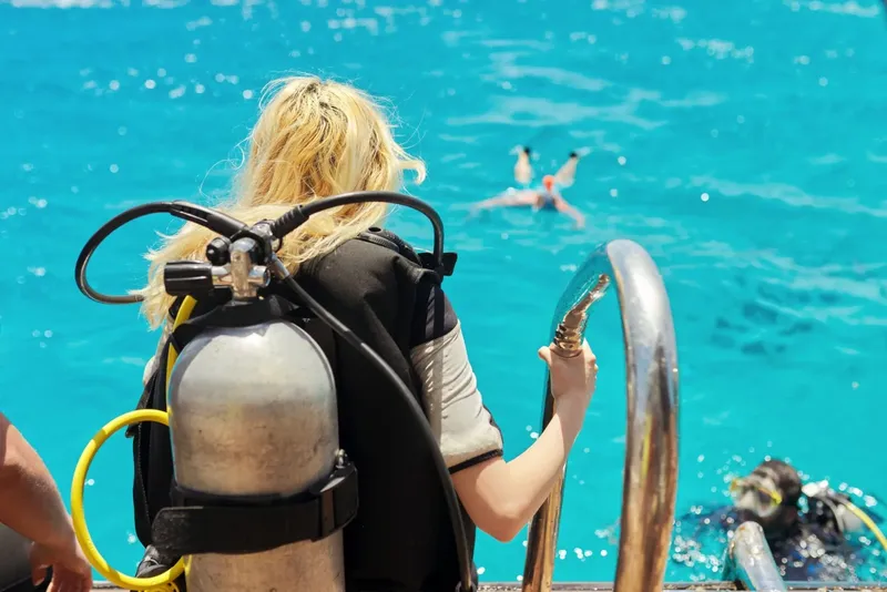 Plongeuse préparant son équipement au bord de l'eau, nageur en arrière-plan