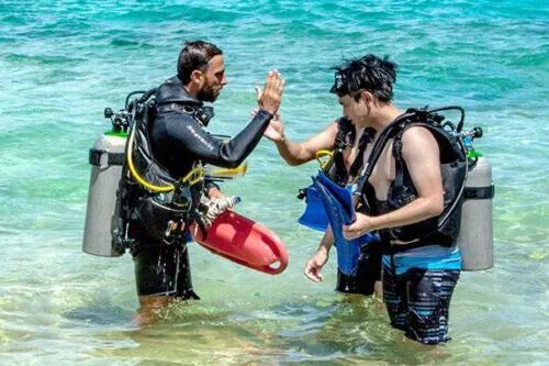 Deux plongeurs s'échangent un high-five sur une plage ensoleillée
