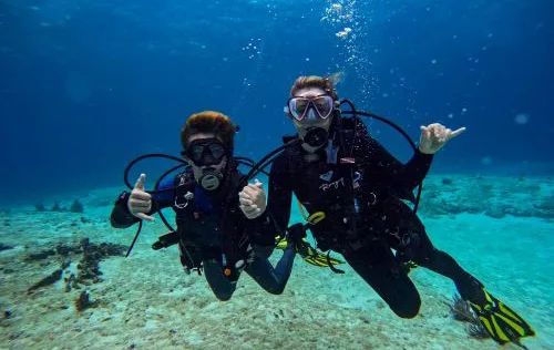 Deux plongeurs souriants font des signes de paix sous l'eau