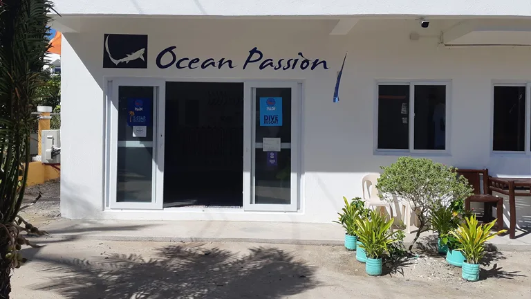 Façade blanche d'un centre de plongée avec enseigne et plantes tropicales