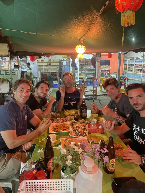 Cinq personnes sourient autour d'une table garnie de nourriture et de bières