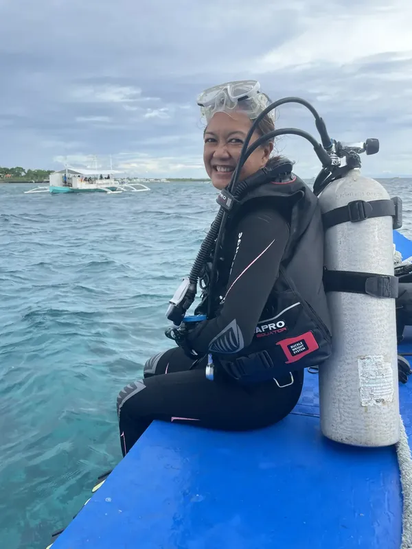 Plongeuse souriante en combinaison, équipée, sur un bateau en mer