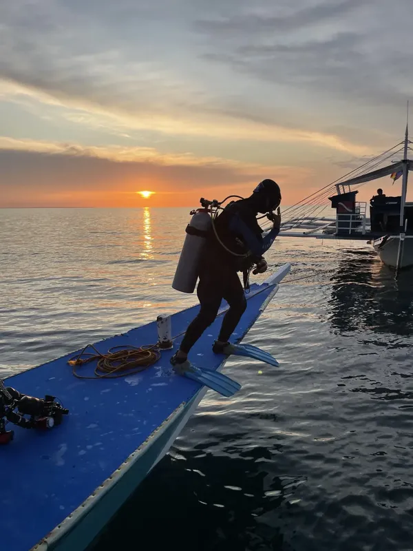 Plongeur s'equipant sur un bateau au lever du soleil en mer