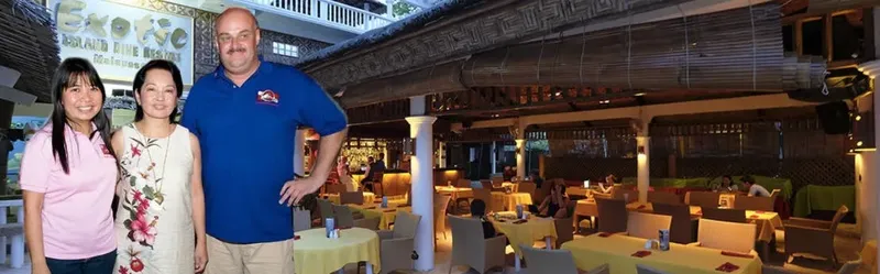 Trois personnes souriantes posent devant un restaurant extérieur éclairé
