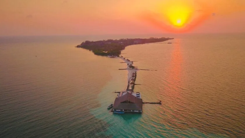 Île tropicale avec ponton d'accès au coucher du soleil sur mer