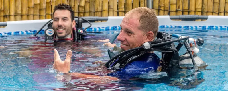 Deux plongeurs souriants en formation dans une piscine avec équipement