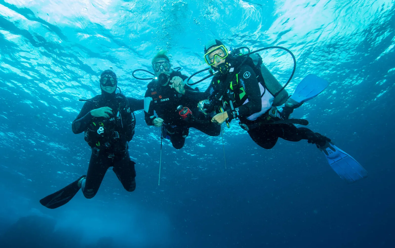 Trois plongeurs en combinaison explorent les fonds marins bleus