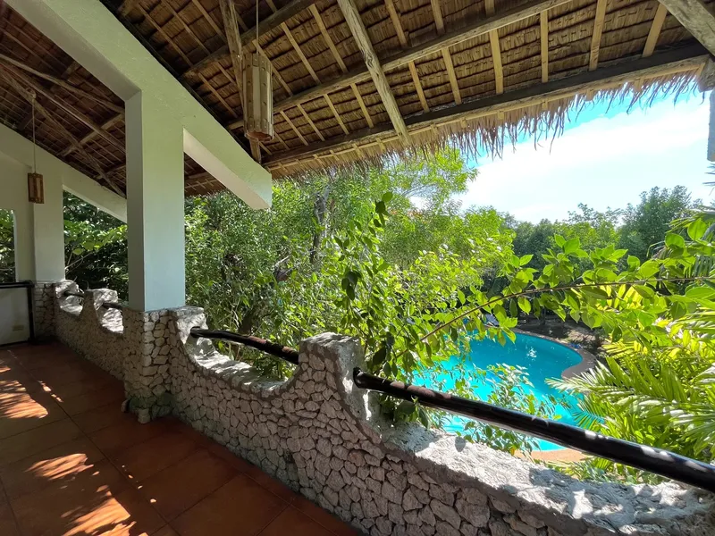 Terrasse couverte avec vue sur une piscine entourée de végétation tropicale