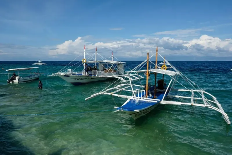 Plusieurs bateaux de pêche et plongeurs sur une mer turquoise ensoleillée